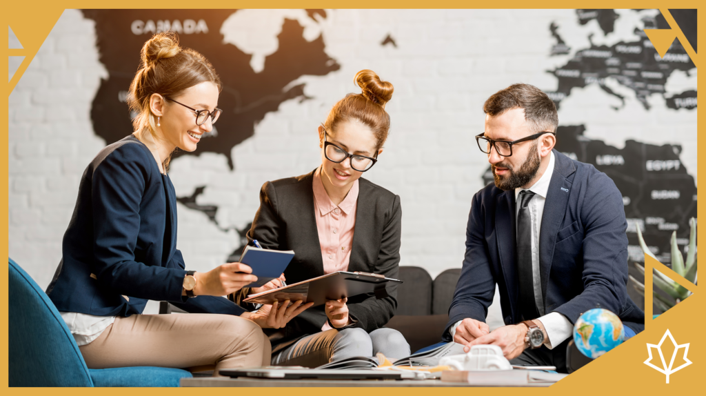 A group of international recruiters sit in a meeting together, in the background on the wall there is a map of the world.