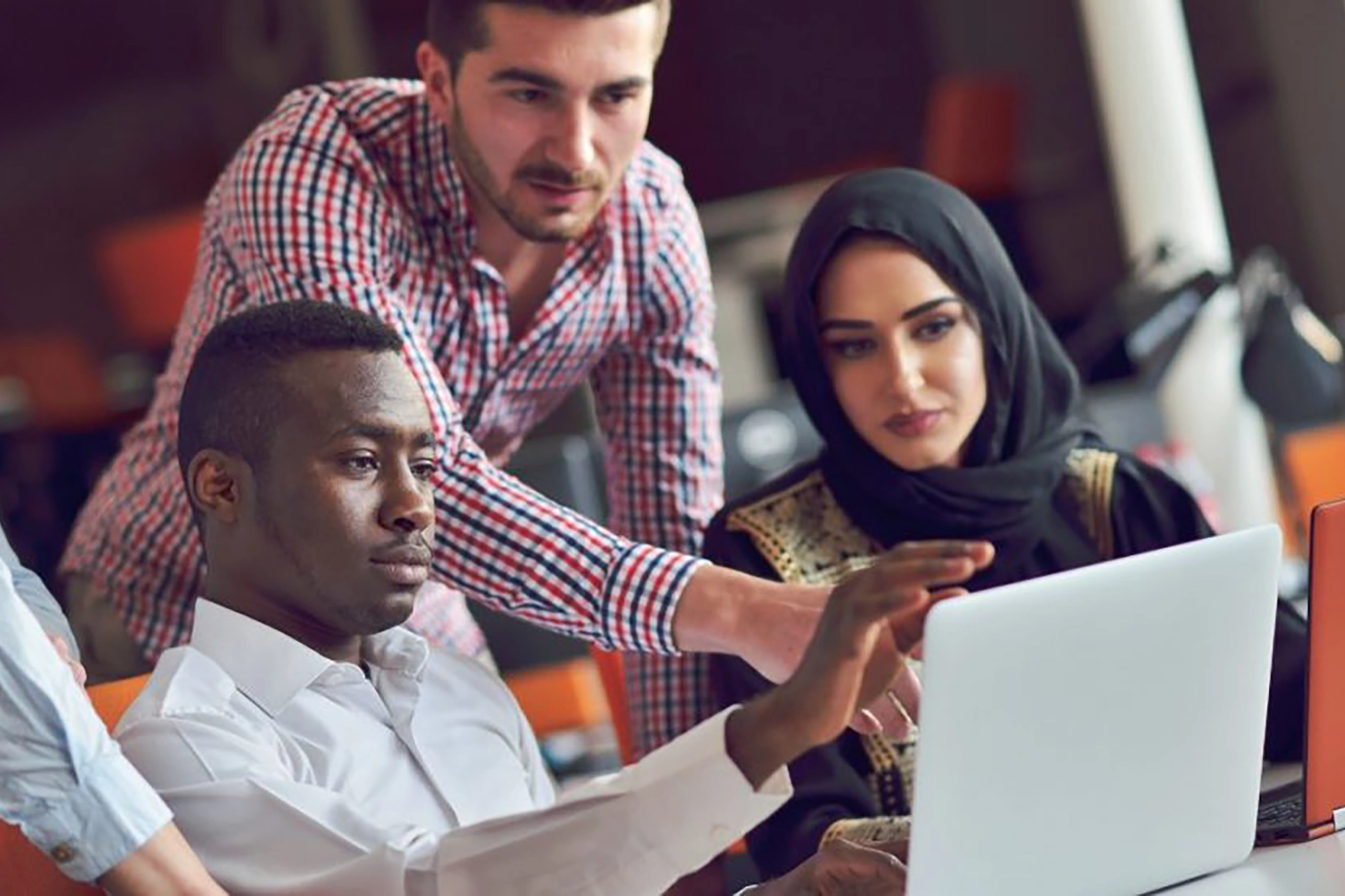 Three employees gather around a computer screen to work on a project together.