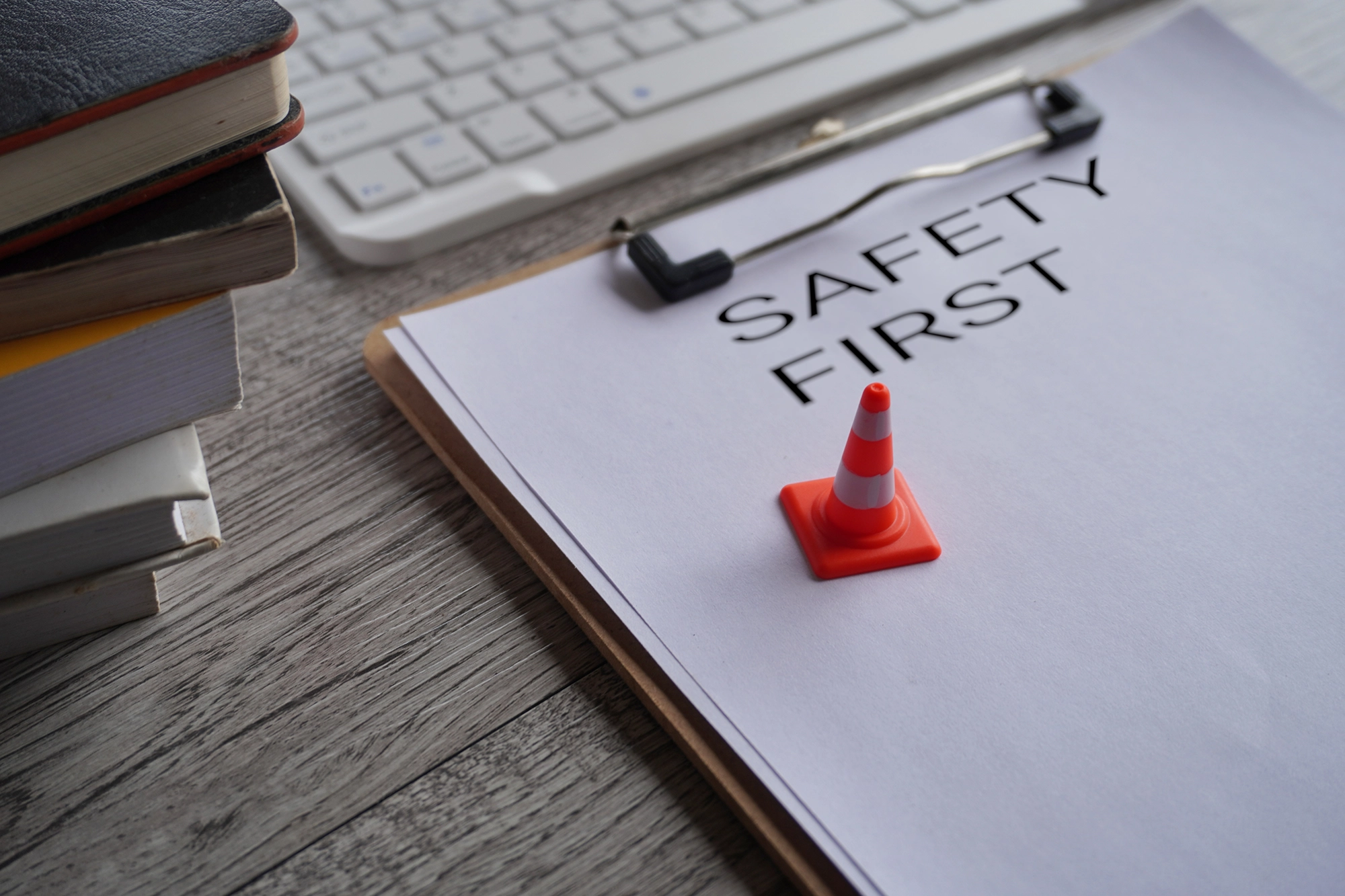 A clip board on a desk with the first sheet of paper reading "safety first." On top is a miniature safety pylon to represent workplace safety.