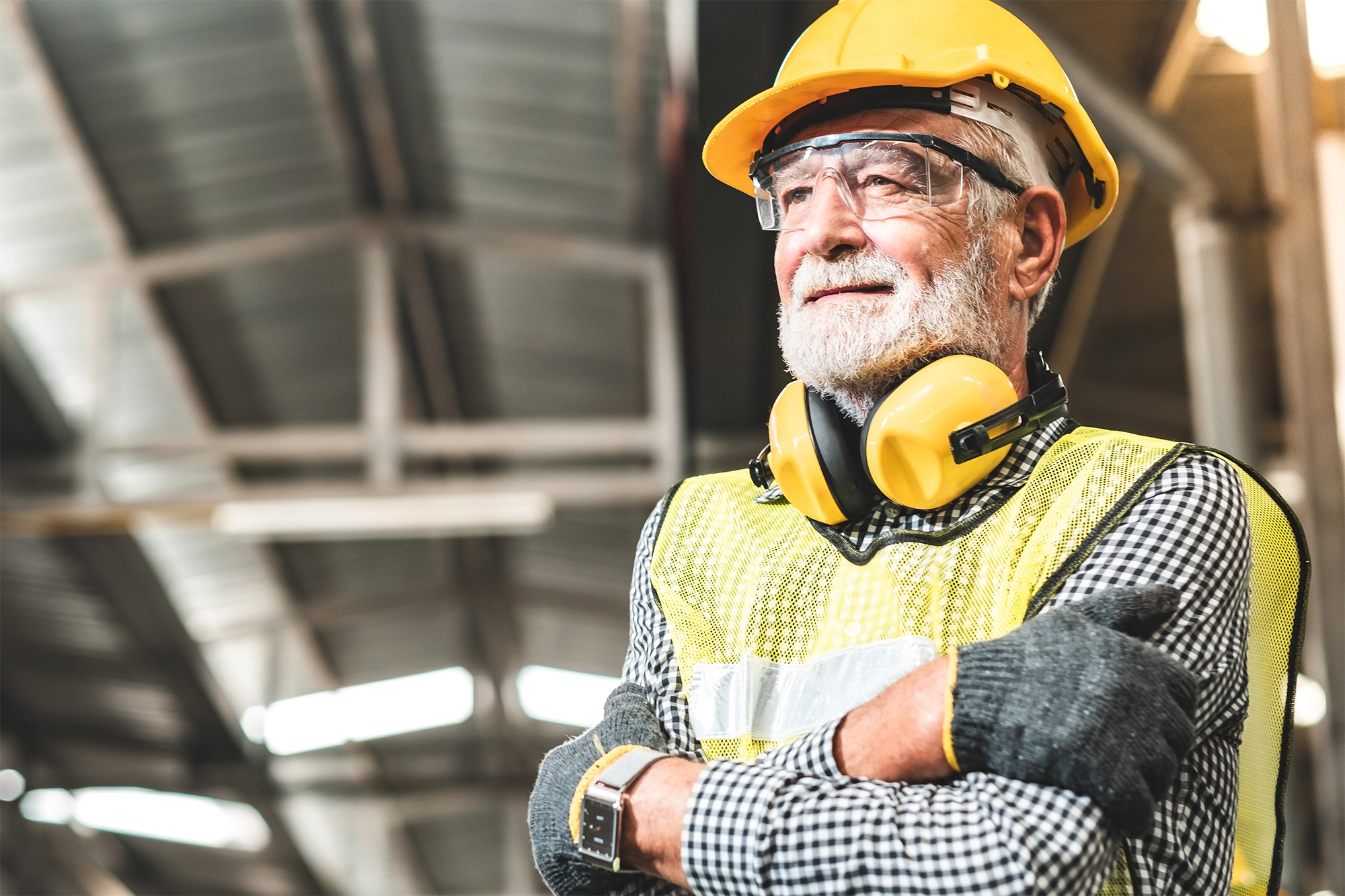 Older man working in a factory setting. He is wearing safety gear including a hard hat.