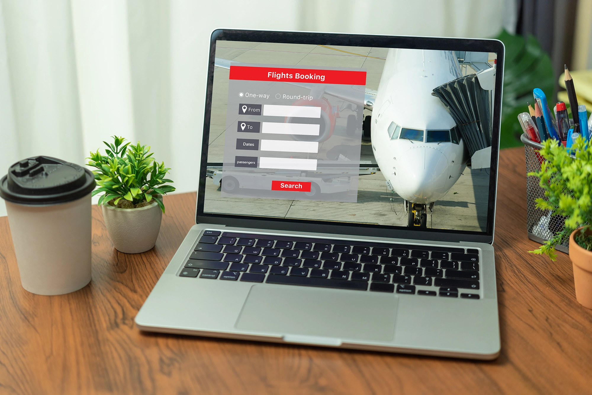 The image features a laptop with a website for booking flights. Next to the laptop the is a cup of coffee and a potted plant.