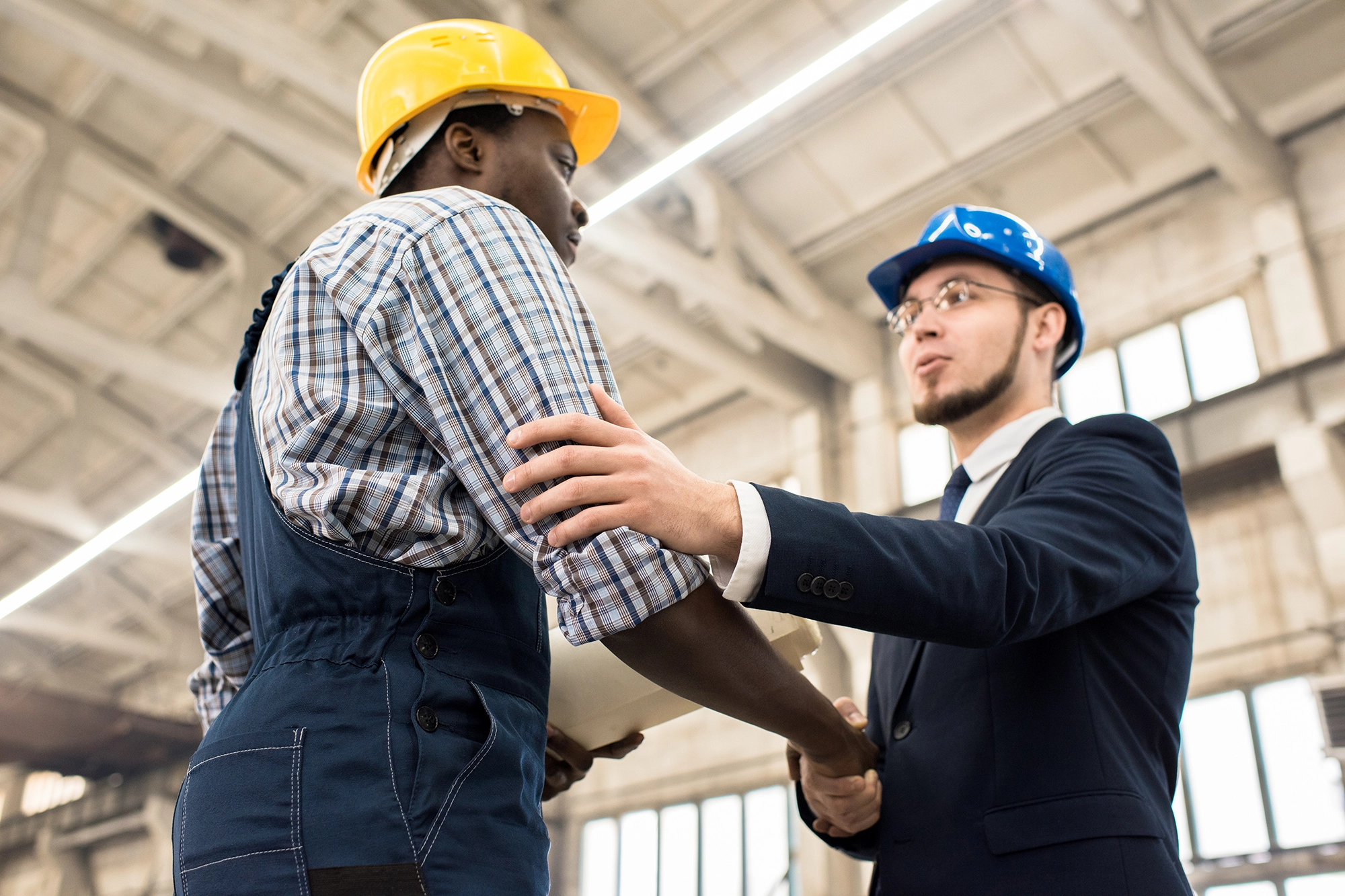 Two workers wearing hard hats greet each other on the job site.