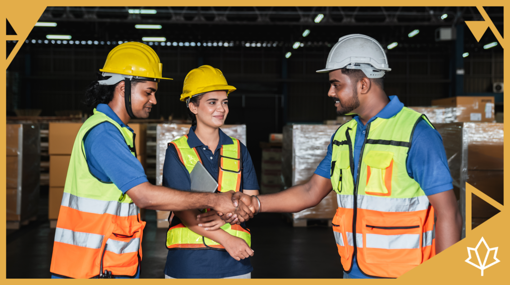 A group of construction workers together on a job site with safety gear on, two of them are shaking hands.