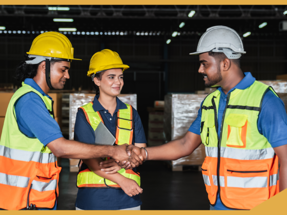 A group of construction workers together on a job site with safety gear on, two of them are shaking hands.