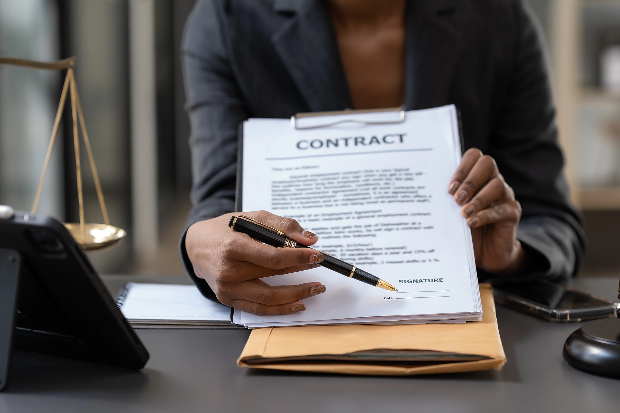 A close-up of a woman in a business suit holding a clipboard with a contract and pointing at the signature section with a pen, with a balance scale in the background.