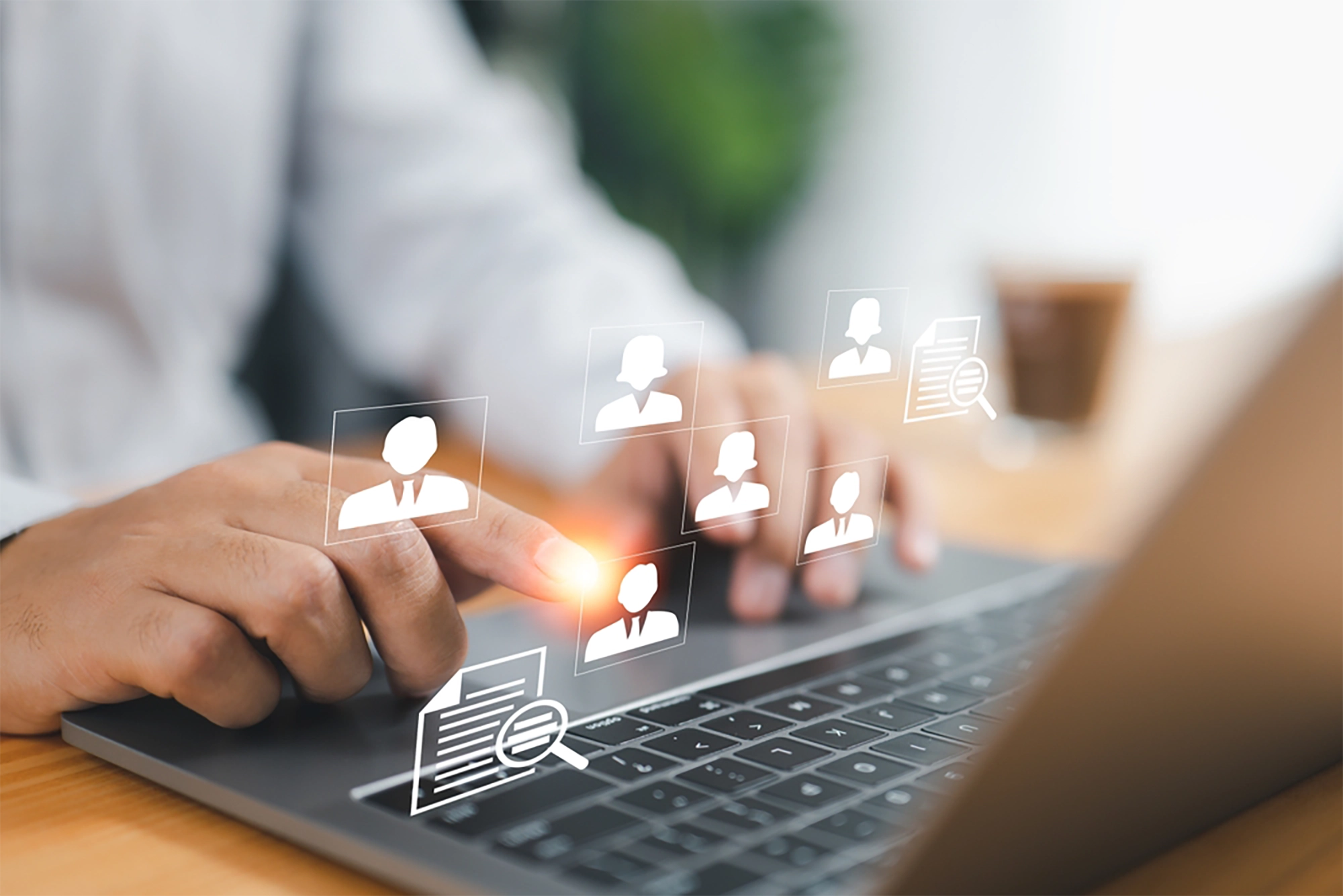 Close-up of a recruiter using a laptop, with their finger touching a digital overlay displaying icons of people and document files, symbolizing virtual recruitment.