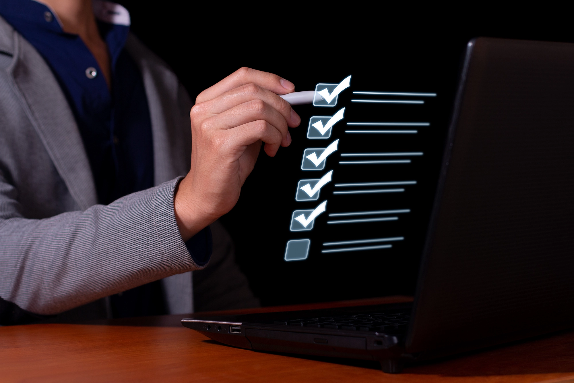 A person in a suit marking a digital checklist on a laptop screen using a stylus, symbolizing task management or document review.